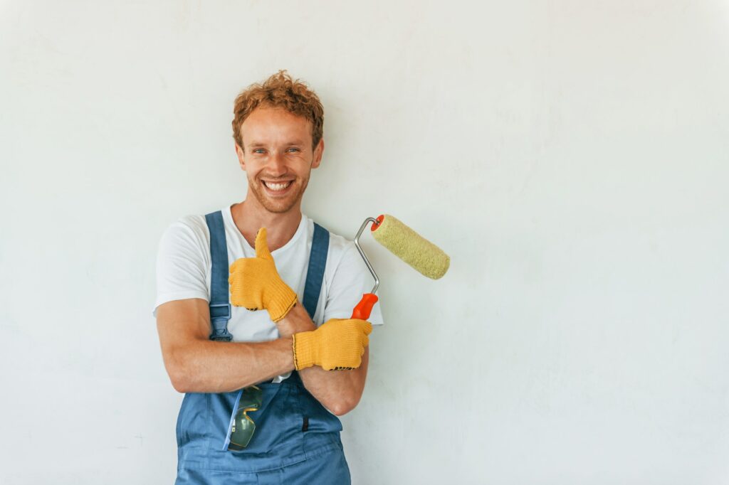 Painting the walls. Young man working in uniform at construction at daytime